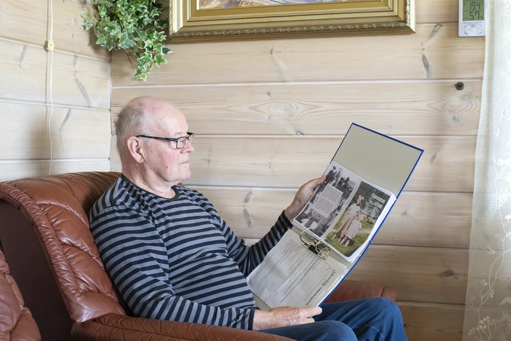 Markku Eskola istuu nojatuolissa ja lukee kansiota, jossa hänen tulevan kirjan teksti on.